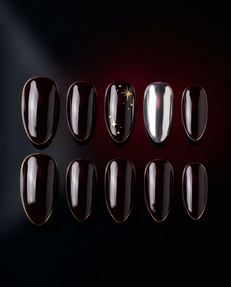 A complete set of ten hand-made press-on nails in deep black-cherry gloss, two with gold star accents and one in mirror chrome