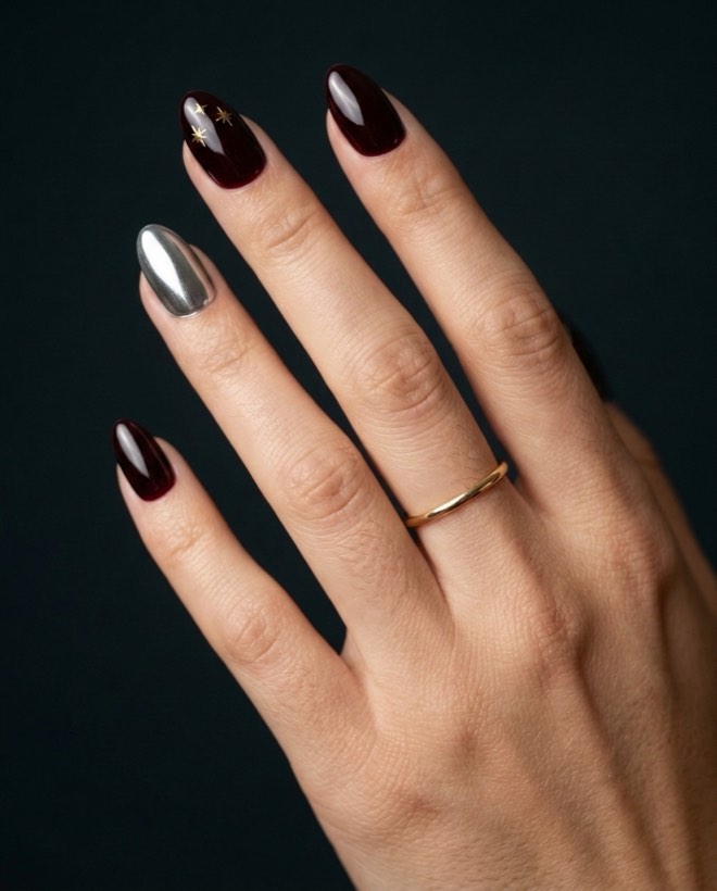 The same hand and the same gold ring, now wearing the black-cherry set with gold stars and one chrome nail